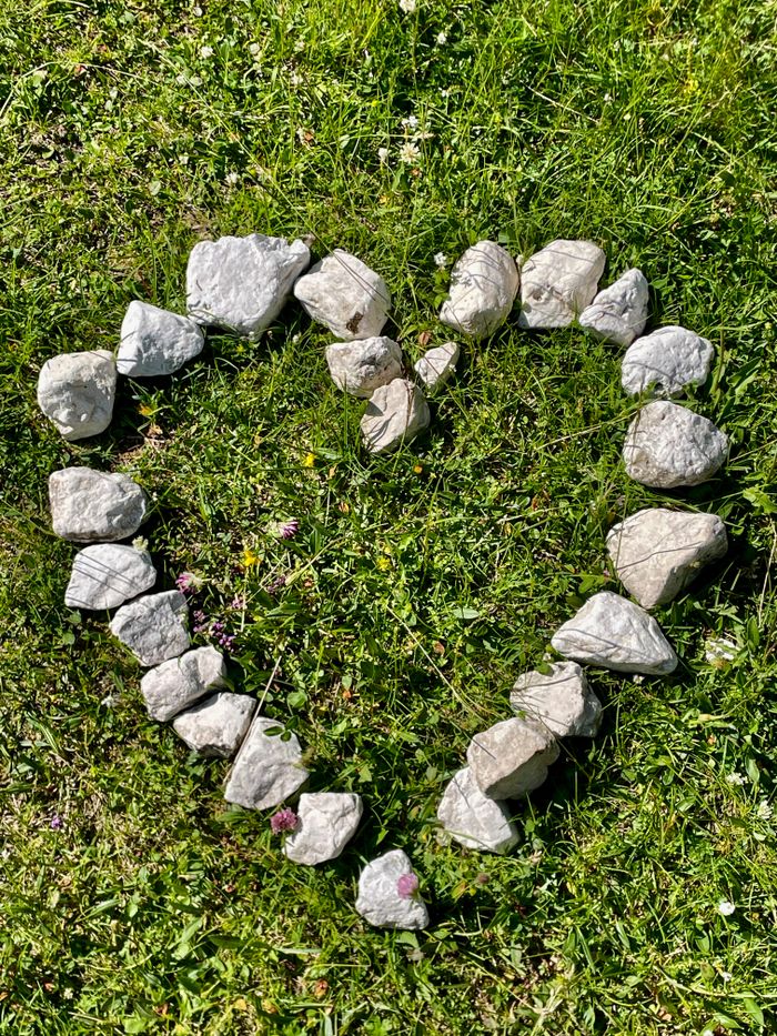 Offerings Heart-shaped stone arrangement on green grass in daylight, symbolizing nature and love.